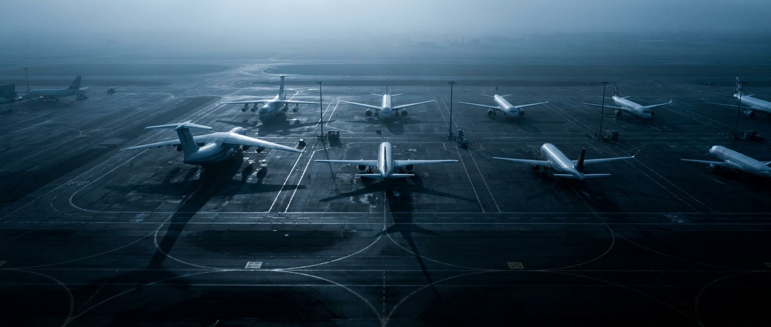 Aircraft parked on an airport apron at dawn, viewed from above in cool low light.